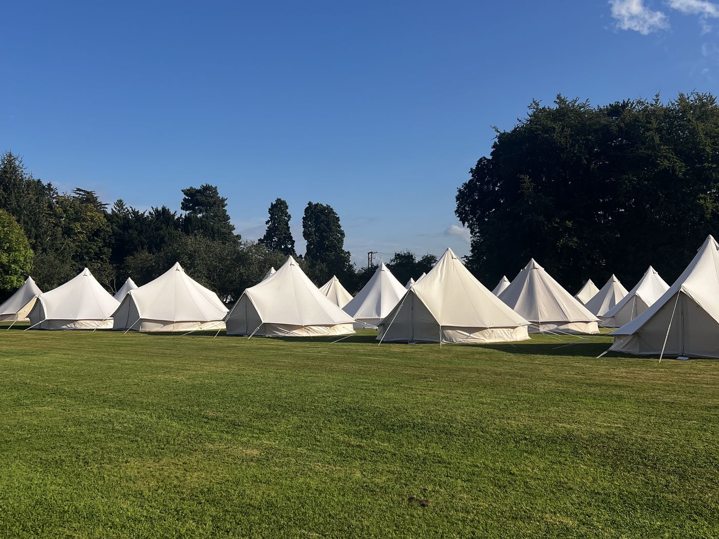 A long row of bell tents on mown grass under a blue sky