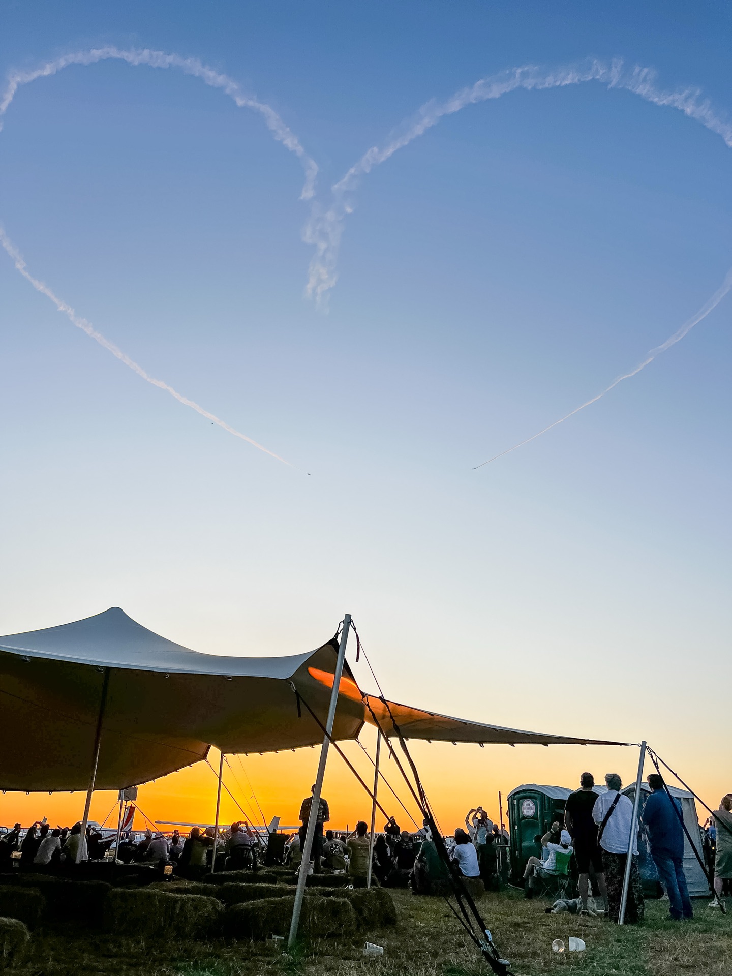 Aerobatic smoke heart drawn in the sky above a stretch tent at sunset