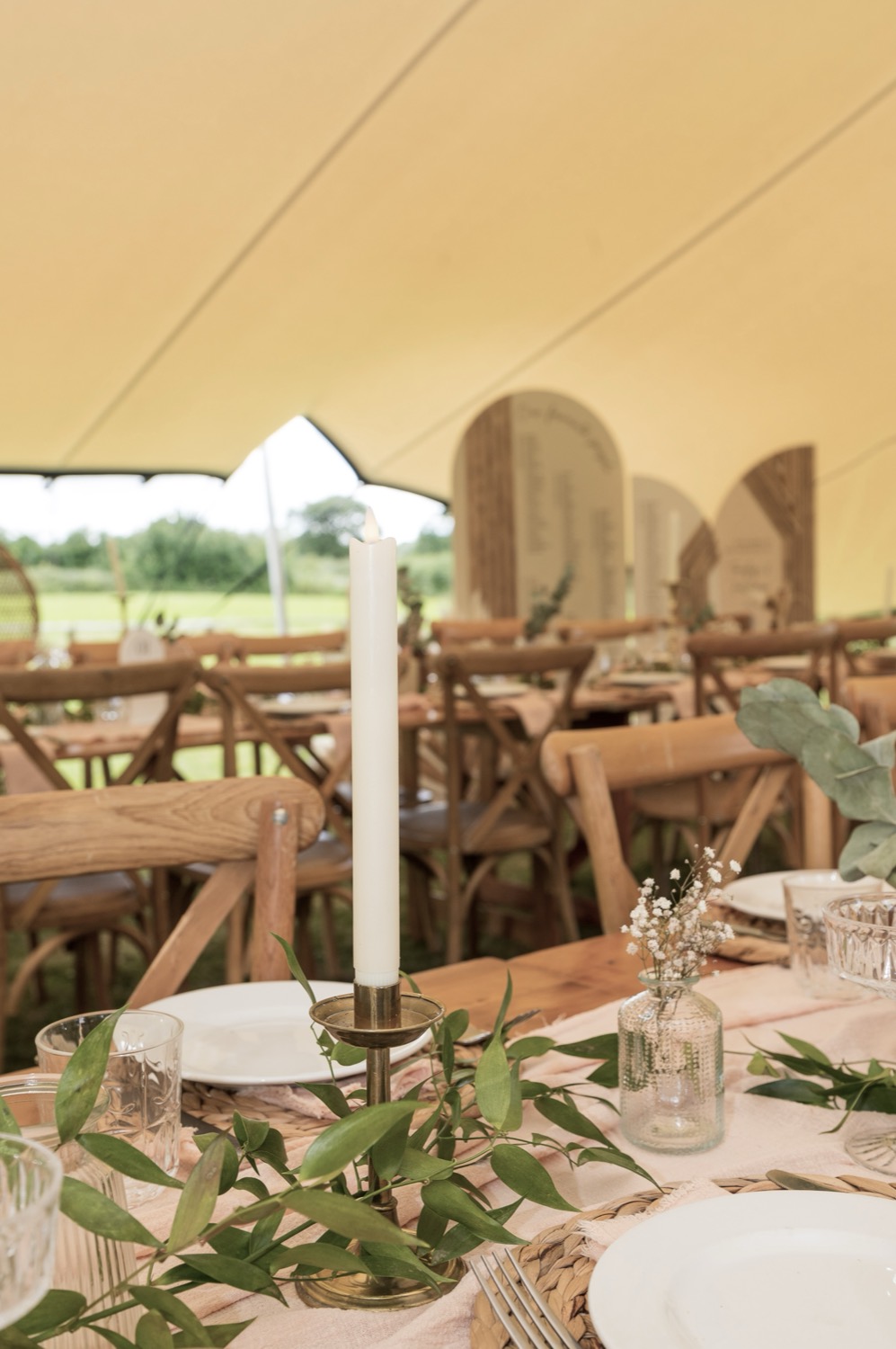 Place setting with a taper candle and eucalyptus runner under a stretch tent