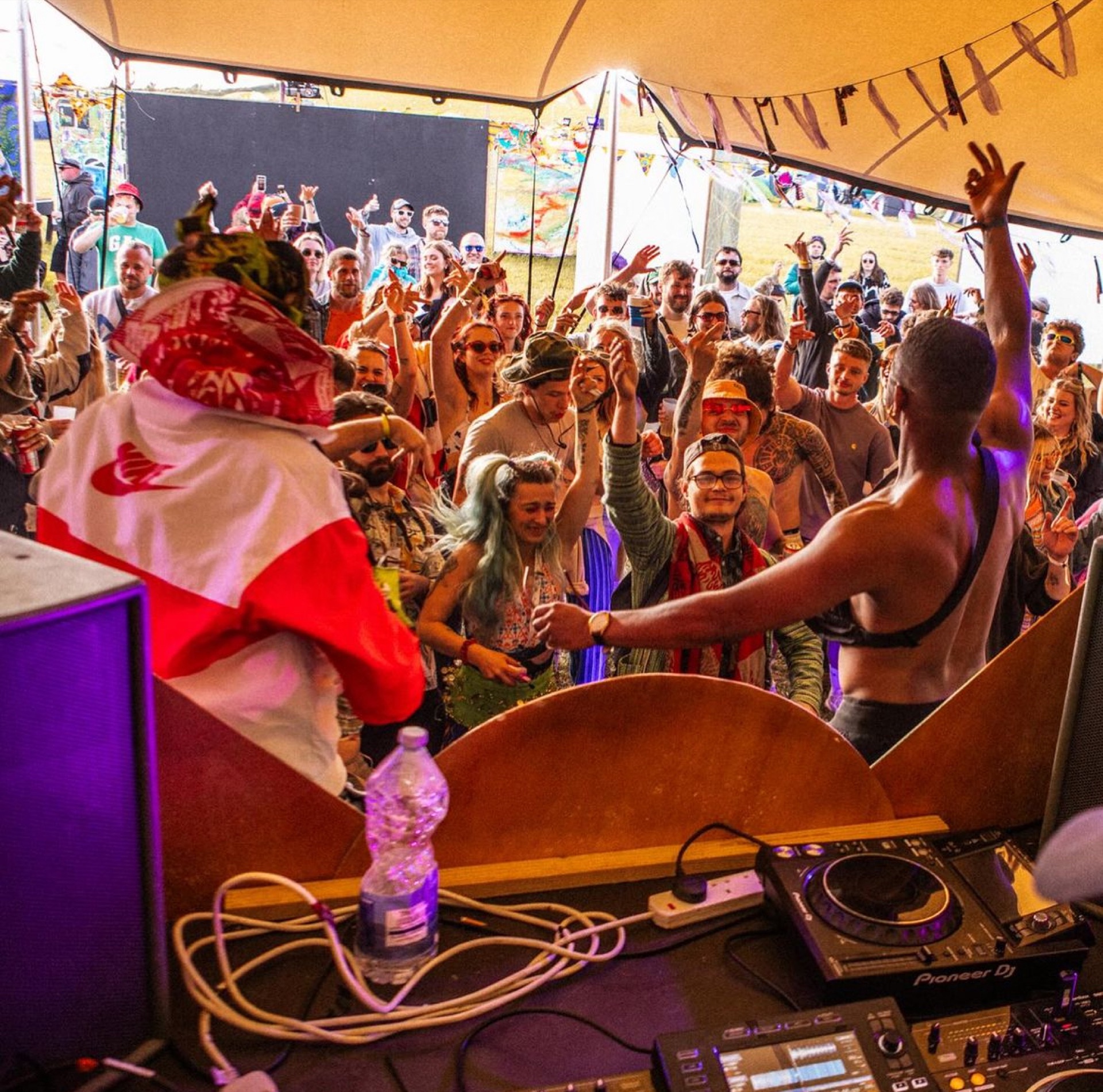 Packed crowd dancing in front of a DJ under a stretch tent at a festival
