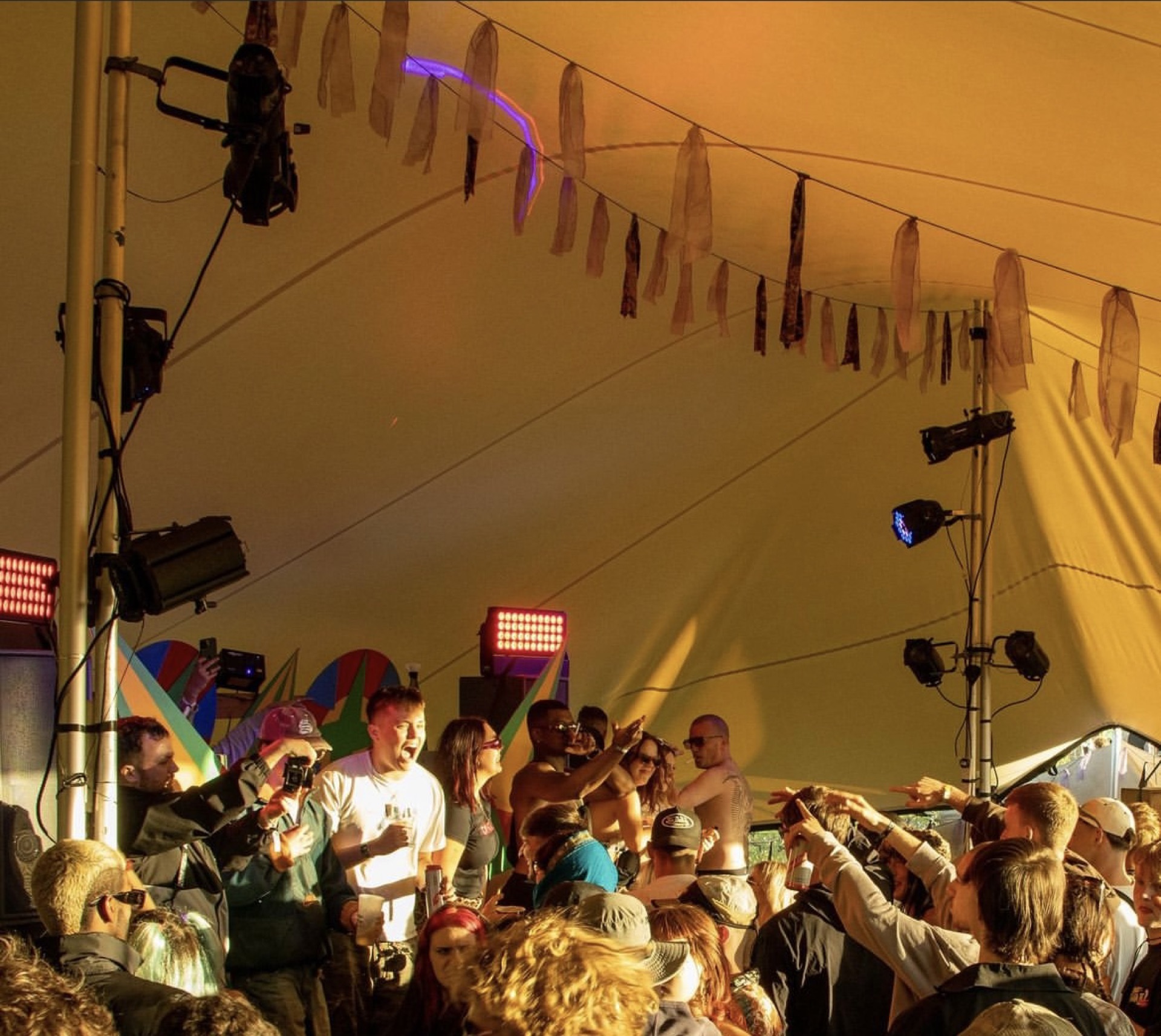 Festival crowd dancing under a stretch tent at night with stage lighting