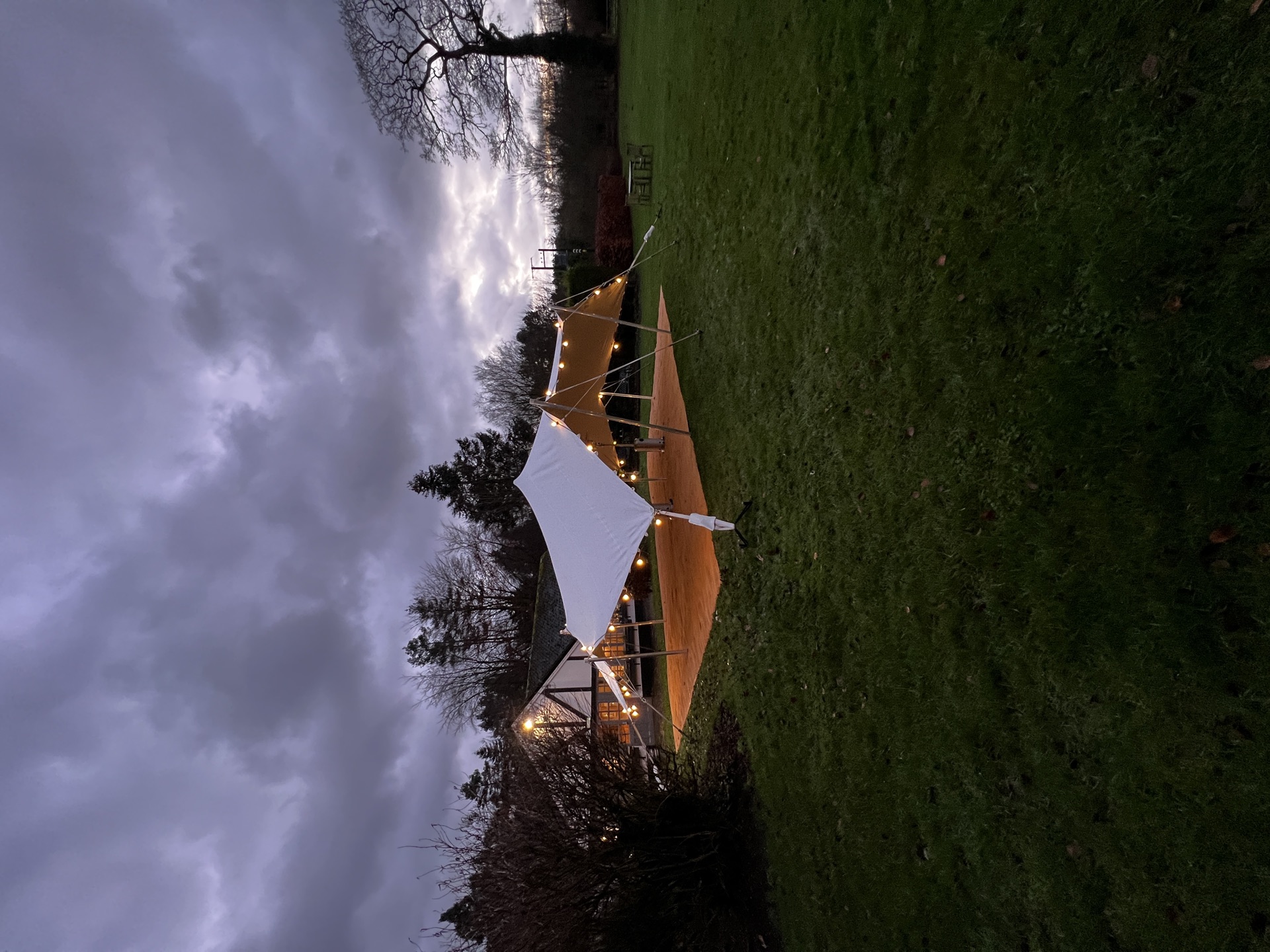 Stretch tent over a wooden dance floor at dusk, lit with festoon