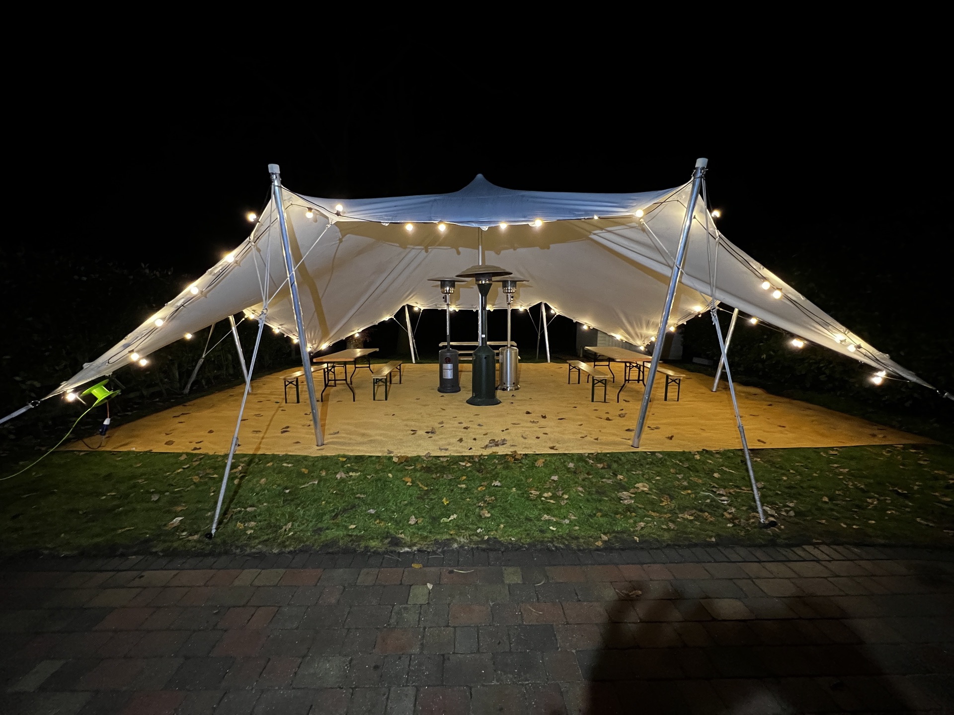 Stretch tent at night with festoon lighting, patio heaters and trestle seating on matting