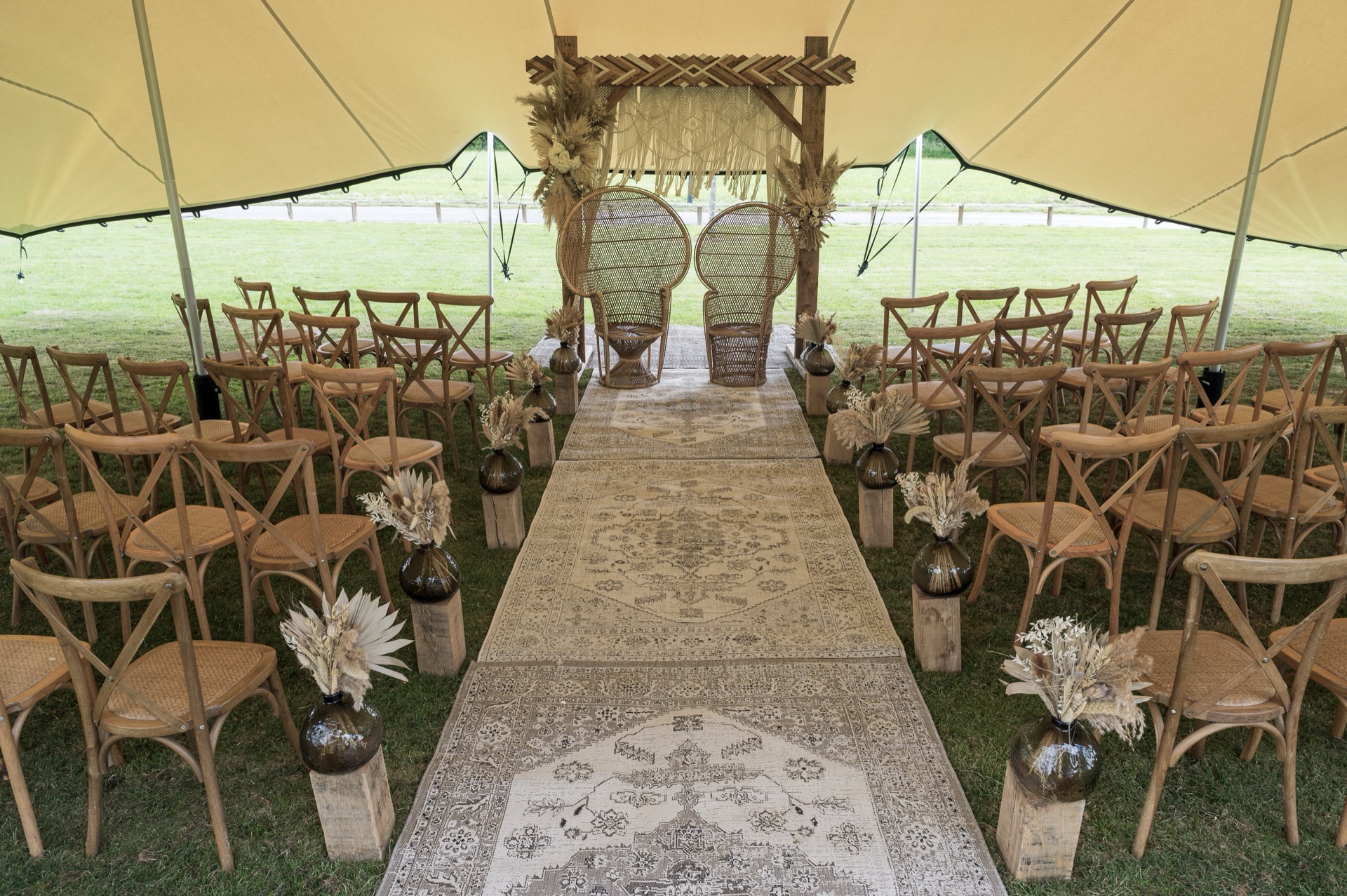 Wedding ceremony aisle under a stretch tent, rug runner leading to a floral arch and peacock chairs
