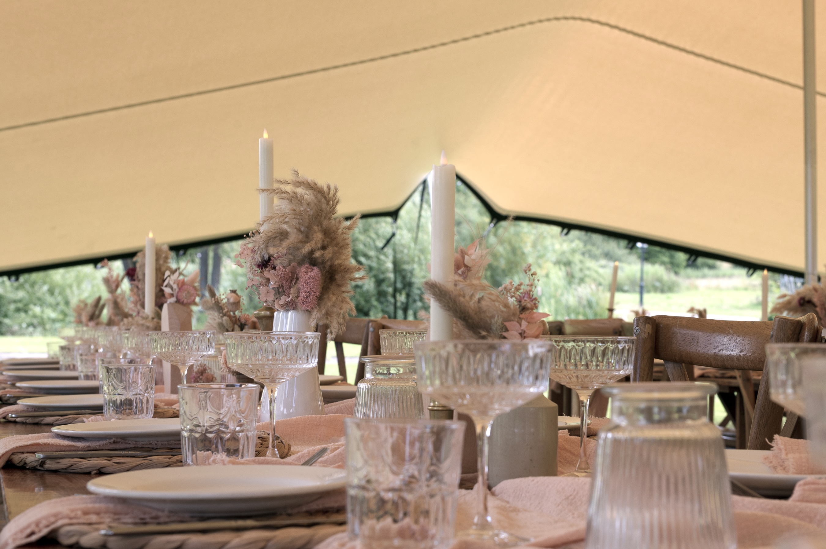 Close-up of cut-glass glassware and place settings on a dressed wedding table under a stretch tent