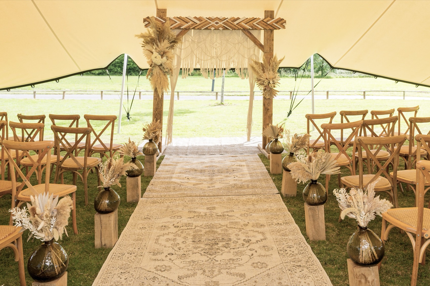 Boho wedding ceremony aisle and macrame arch under a stretch tent