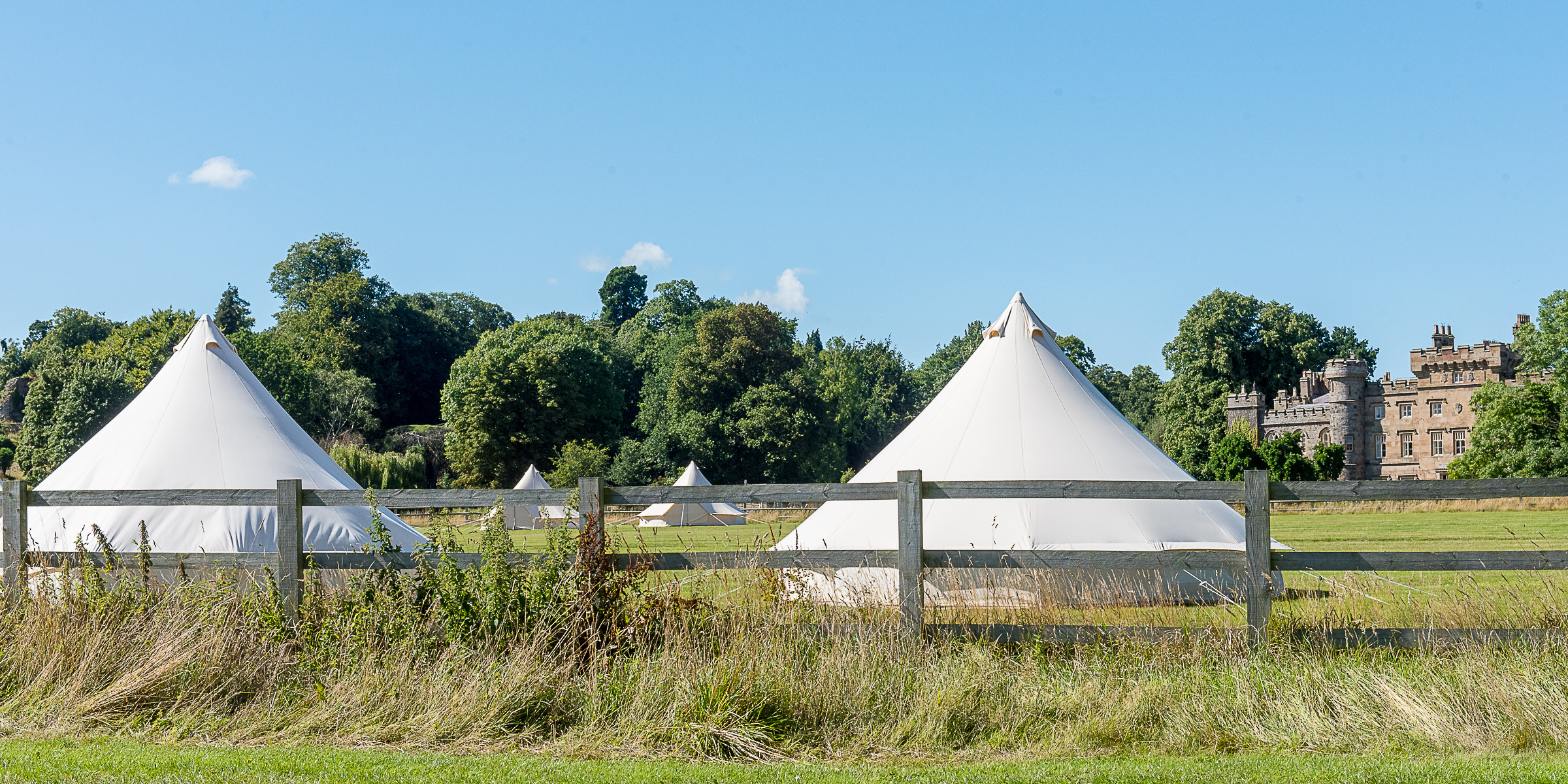 Bell tents pitched in parkland with Hawarden Castle behind