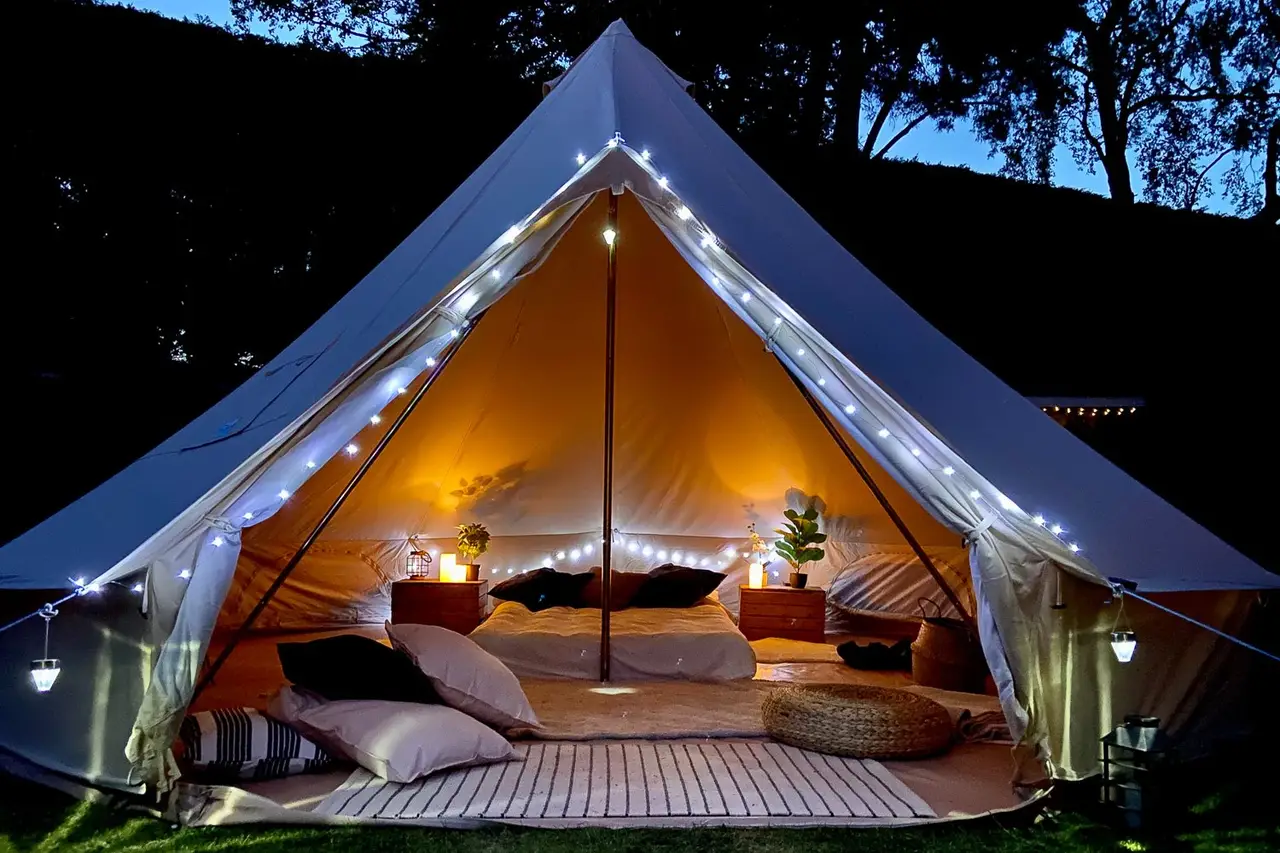 Bell tent glowing after dark, beds made up inside