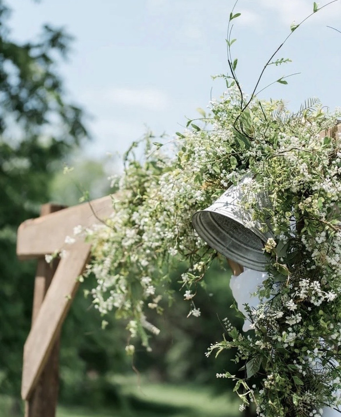 A decorative bell wrapped in white blossom on a wedding arch
