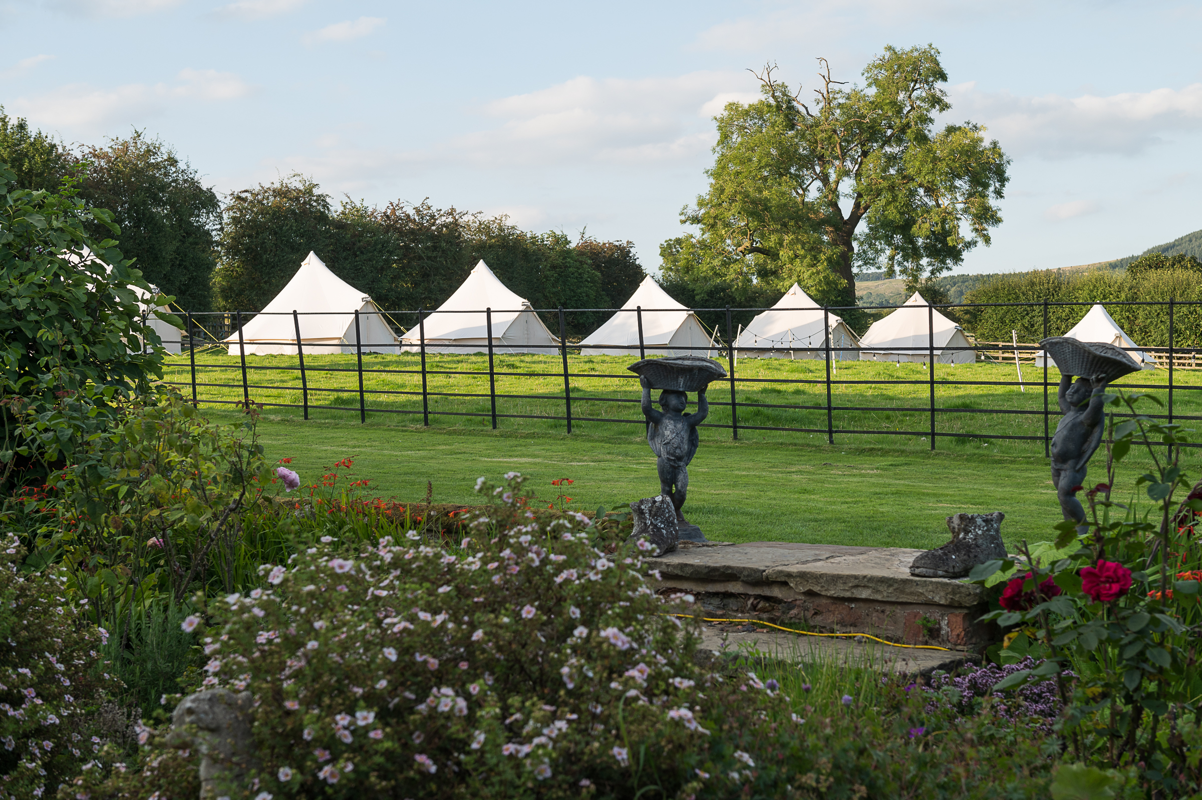 A bell tent village behind a cottage garden, hills beyond